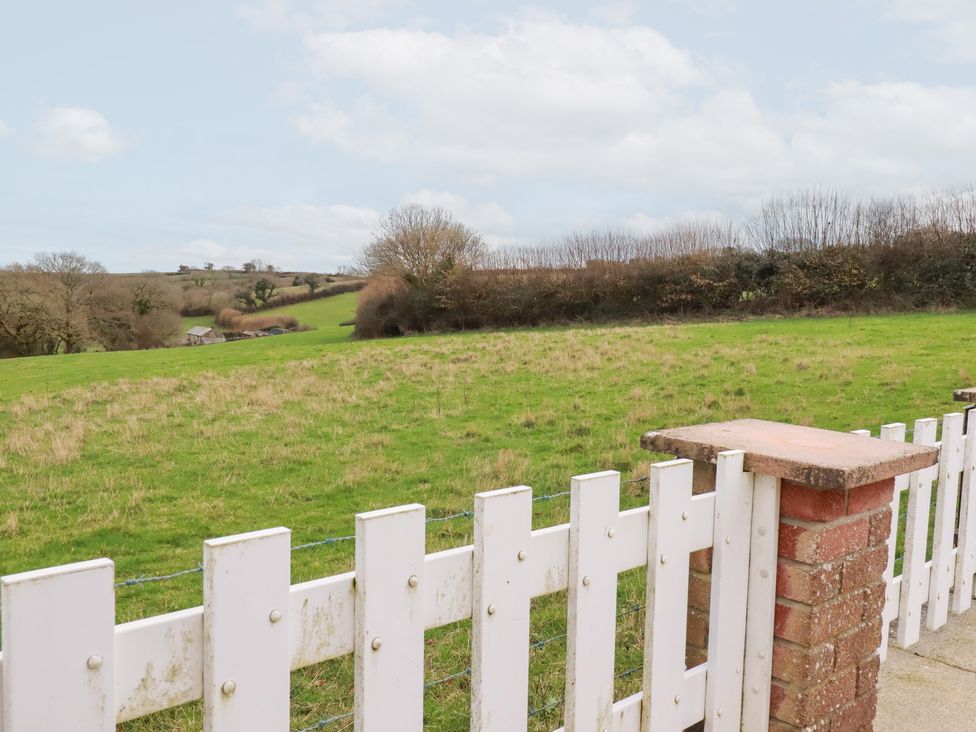 A view of a grassy field and trees beyond a white fence at The Bungalow in St. Austell