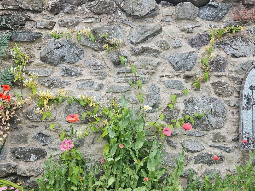 A stone wall with flowers and plants at Katie's Cottage in Church Stretton