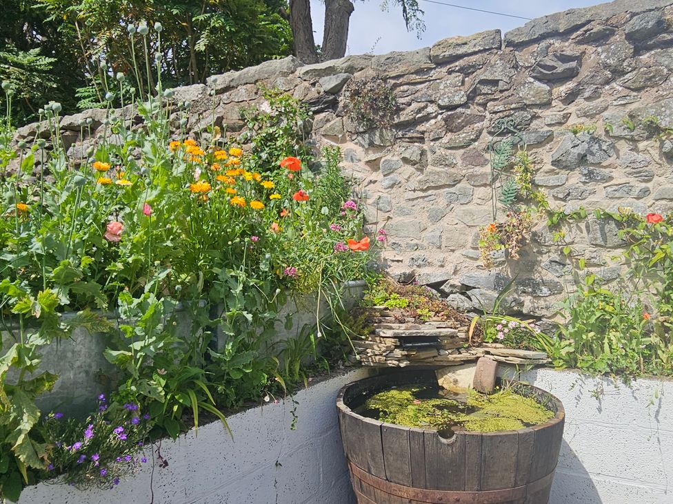 A garden with flowers and a wooden barrel near a stone wall at Katie's Cottage Church Stretton