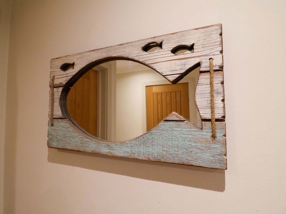 A mirror with a fish-shaped wooden frame in the hallway at Cliff Cottage