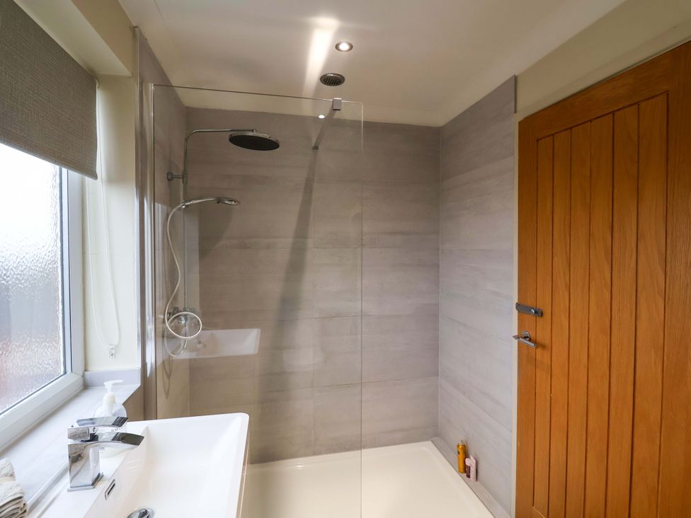 A bathroom with a shower, sink, and door at Cliff Cottage