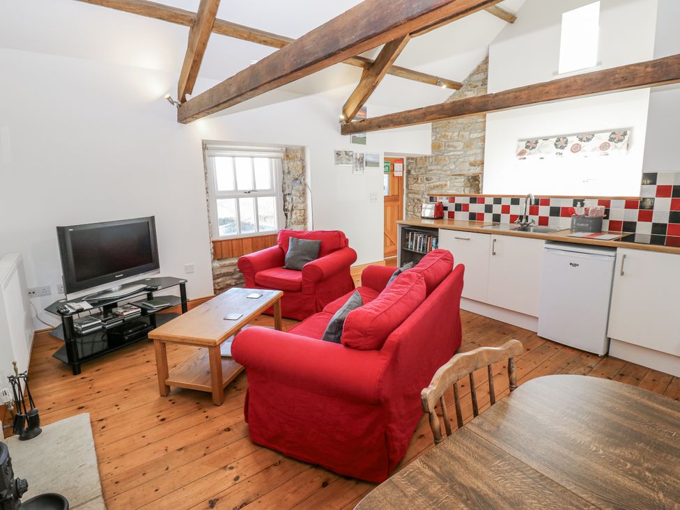 A living room with a television and red sofas at Dove Cottage in Hexham