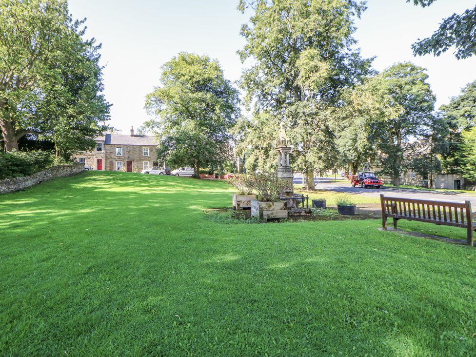 An outdoor area with grass, trees, a bench, and a monument at Dove Cottage in Hexham