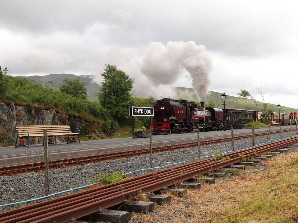 A steam train at a station with a bench and sign at Rhyd Ddu in Caernarfon
