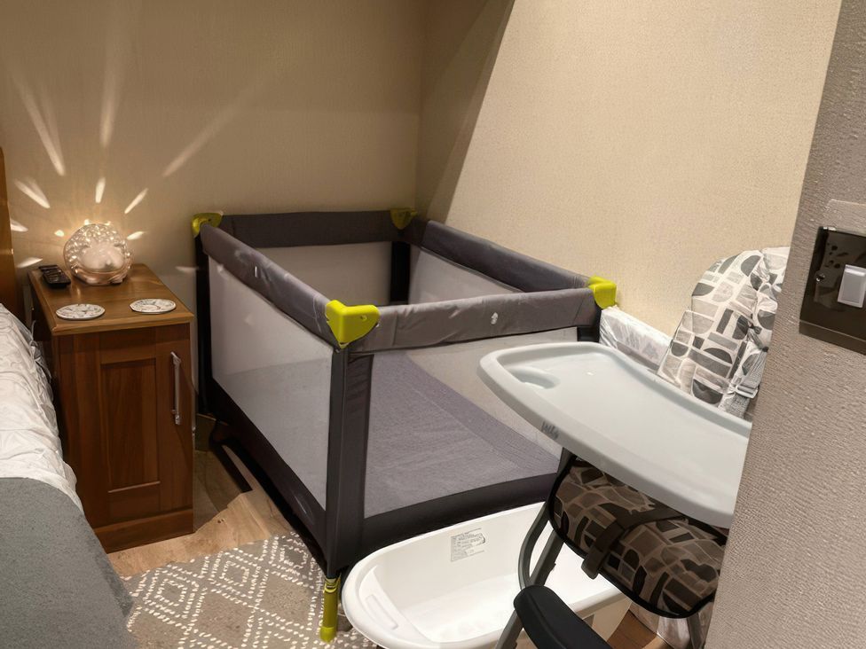 A bedroom with a crib and a chair at Tiggywinkle Beck - White Cross Bay Windermere