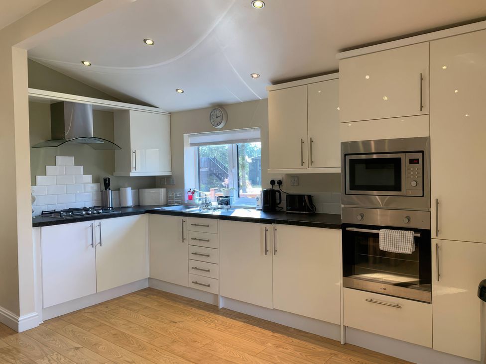A kitchen with cabinets, stove, oven, and window at Owls House - White Cross Bay Windermere