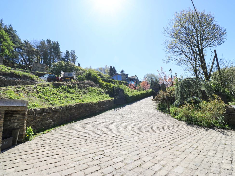A paved road leading to a gate with trees and vehicles at Rocks Cottage in Halifax