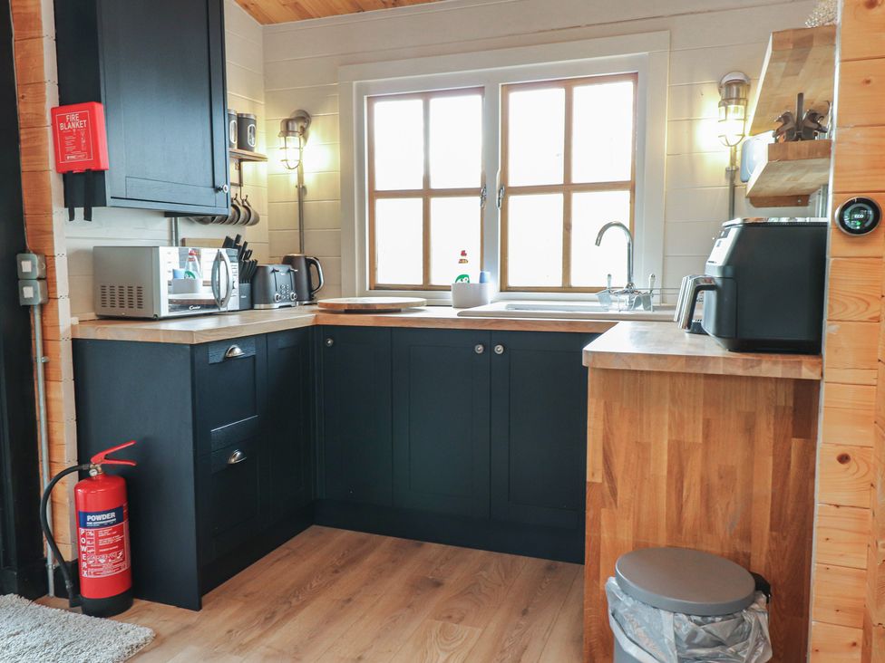 A kitchen with a sink, microwave, and kettle at Caban Tan Y Dderwen in Chwilog