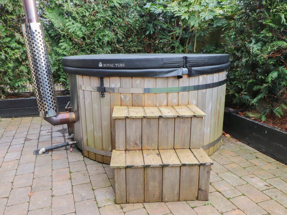 A hot tub with wooden steps on a brick patio at Caban Tan Y Dderwen in Chwilog
