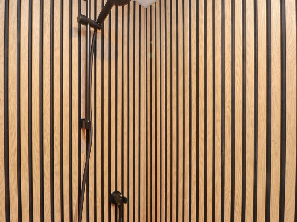 A bathroom with wooden striped wall and shower fittings at Riverside Lodge Afonwen