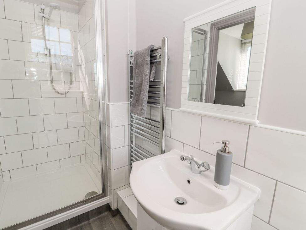 A bathroom with a shower, sink, towel heater, and mirror at Sunset Point in Alnwick