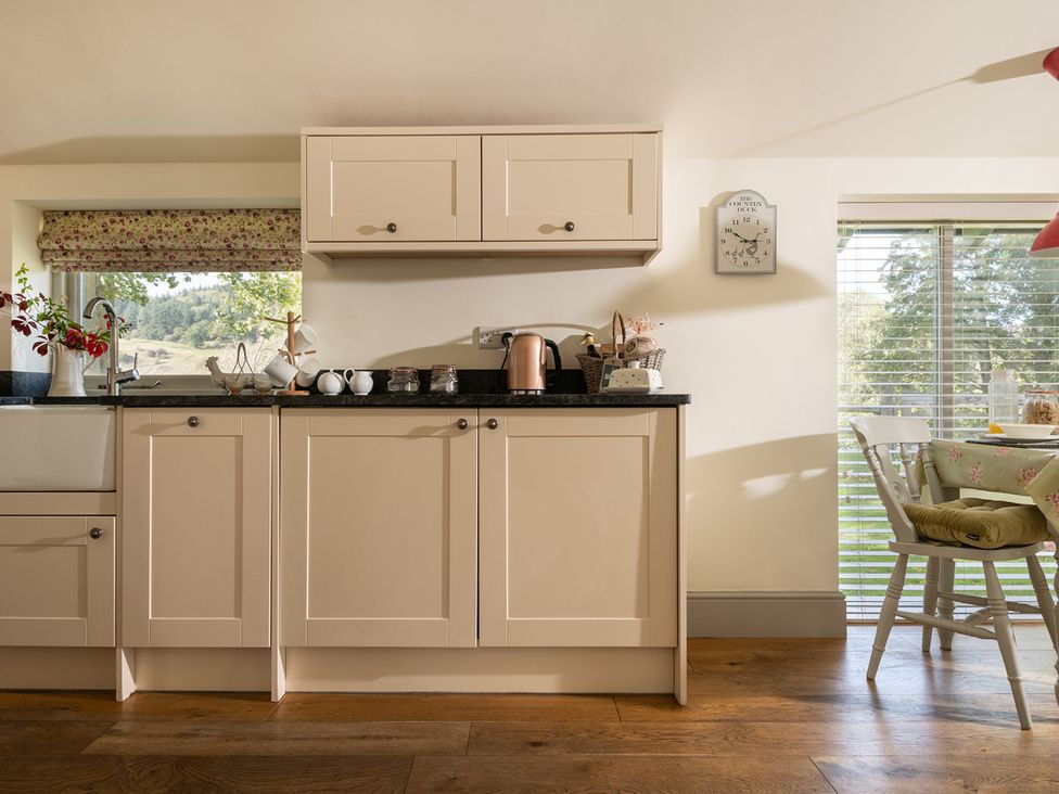 A kitchen with cabinets, sink, kettle and dining area at Ghillies Cottage in Llandrillo