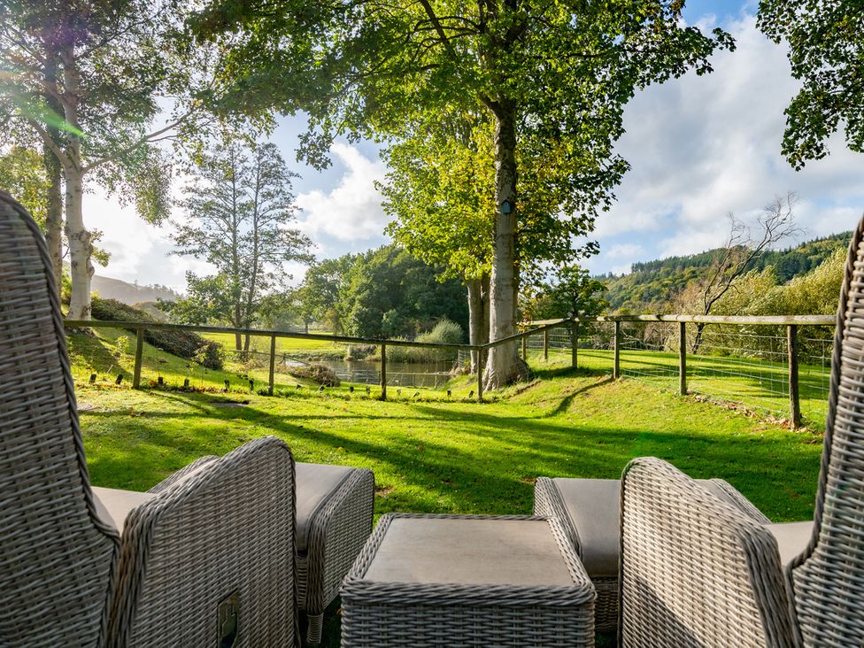 A garden with chairs and a table overlooking a pond at Ghillies Cottage in Llandrillo