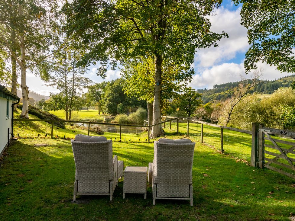 A garden with chairs and a table overlooking a lake at Ghillies Cottage Llandrillo