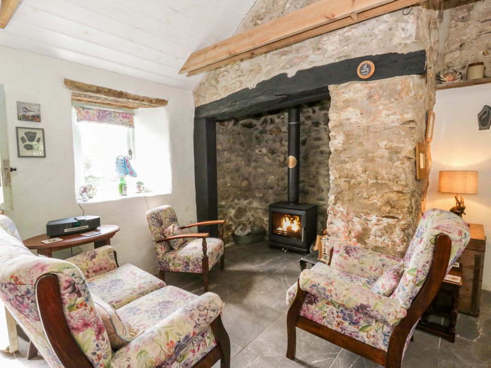 A living room with a wood stove and floral armchairs at Rhos Y Clegyrn in Goodwick