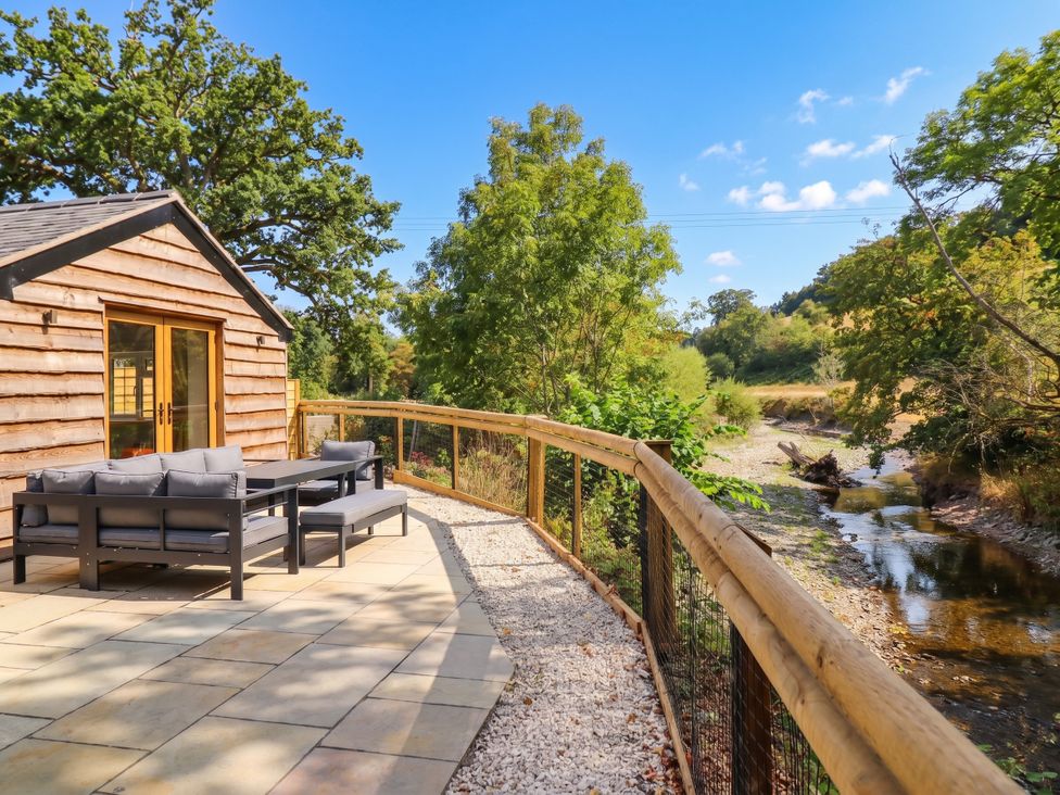 An outdoor area with a cabin and seating by a river at Bridge Farm in Pontyblew near Chirk