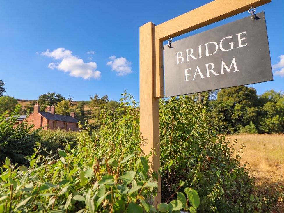A sign for Bridge Farm with a farmhouse in the background at Bridge Farm Pontyblew near Chirk