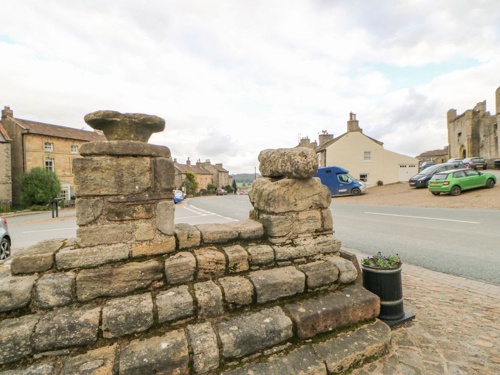 A stone wall and planter with buildings and vehicles in view at In & Out Cottage Leyburn