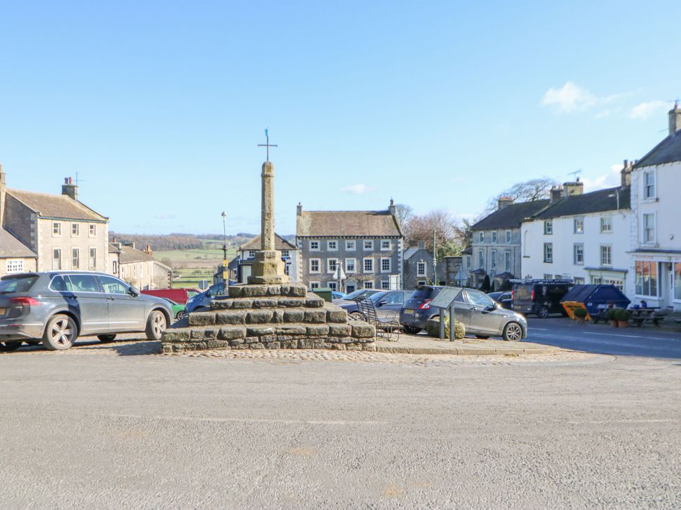 A village square with a stone cross and parked cars at In & Out Cottage Leyburn