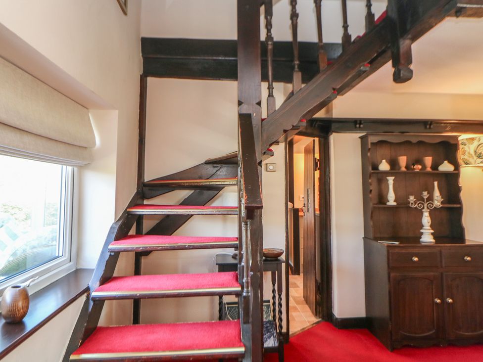 A stairway with red carpet and wooden banister at Pine Cottage 