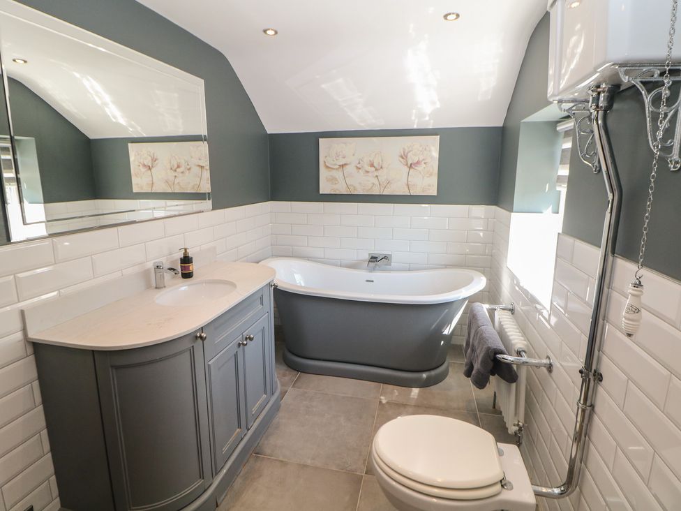 A bathroom with a bathtub, vanity, mirror, and toilet at Pine Cottage