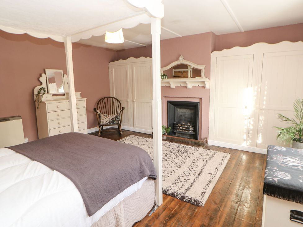 A bedroom with a bed, dresser, chair, and fireplace at Englewood Cottage in Hexham