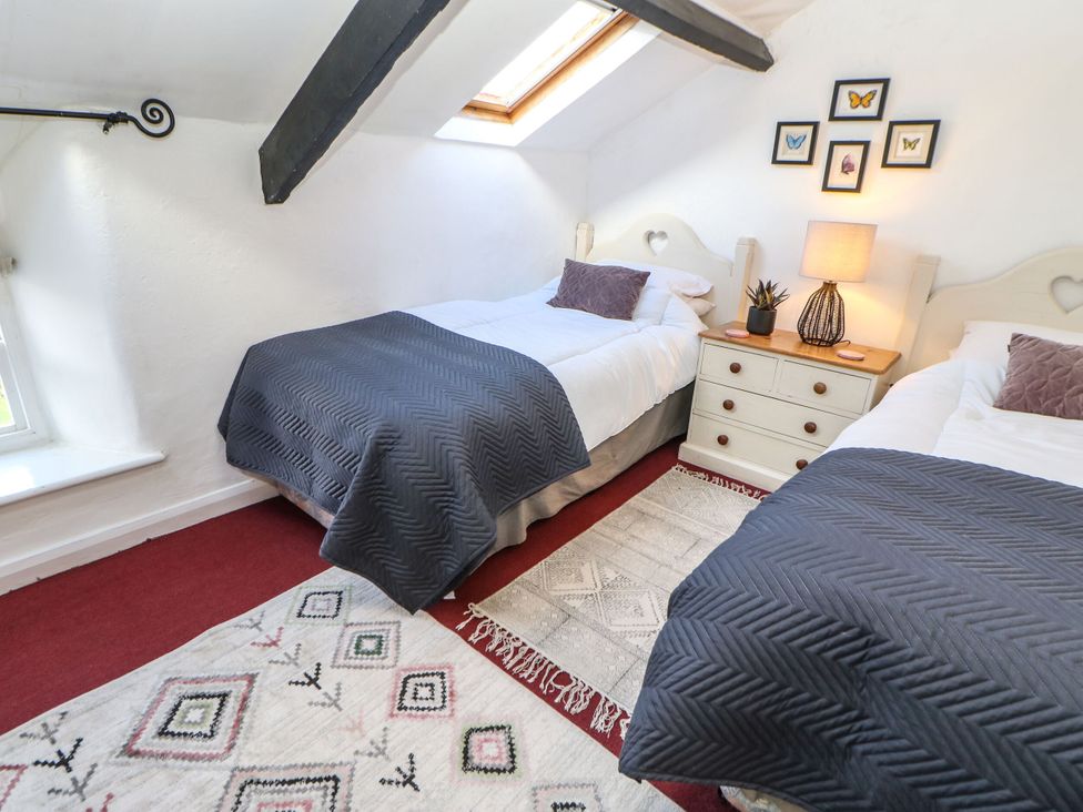 A bedroom with two beds, a nightstand, and a window at Englewood Cottage in Hexham