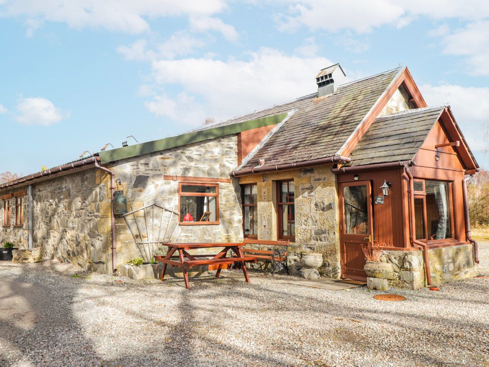 A stone cottage with a table and benches outside at Islay Cottage in Kincraig