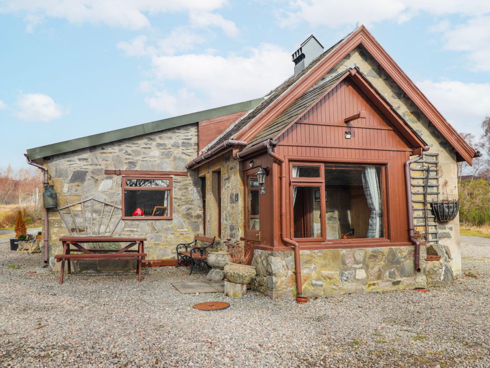 A cottage with a table and chairs next to gravel at Islay Cottage in Kincraig