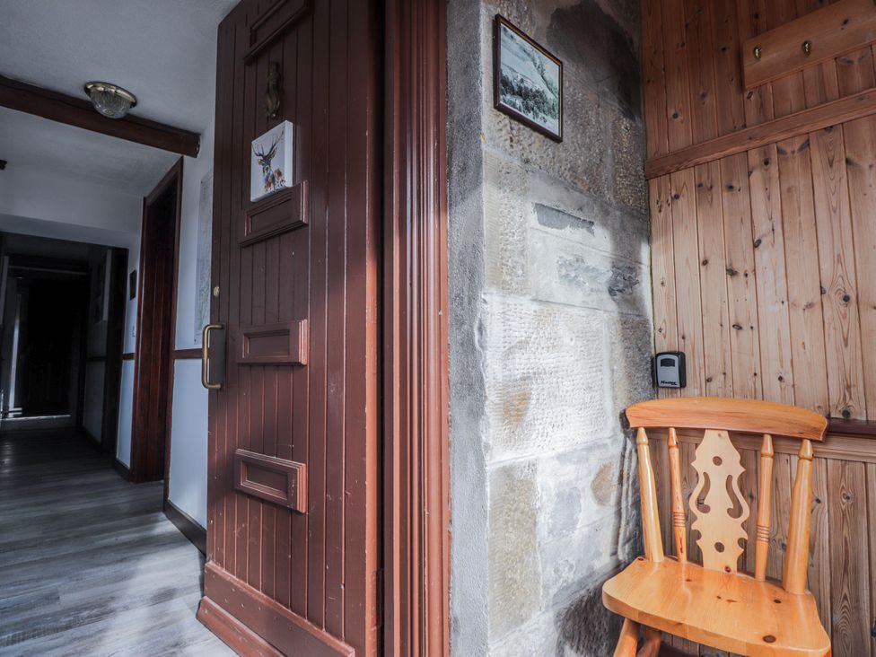 A hallway with a door and wooden chair at Islay Cottage in Kincraig