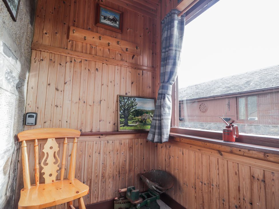 A snug with a chair, picture, window, pot, and wheelbarrow at Islay Cottage, Kincraig