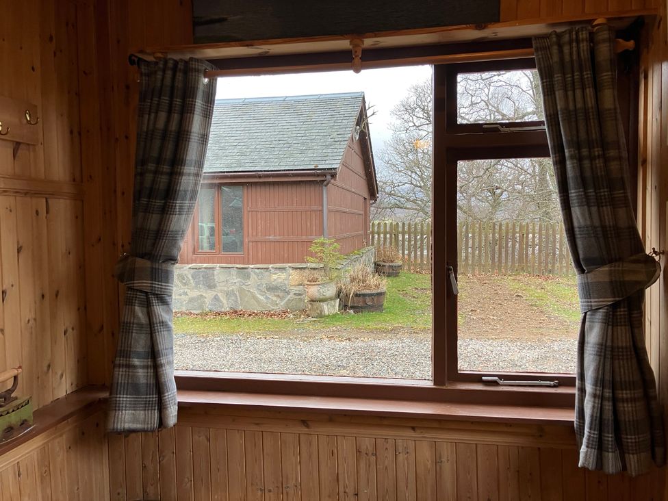 A view from a window showing a wooden building and garden at Islay Cottage Kincraig