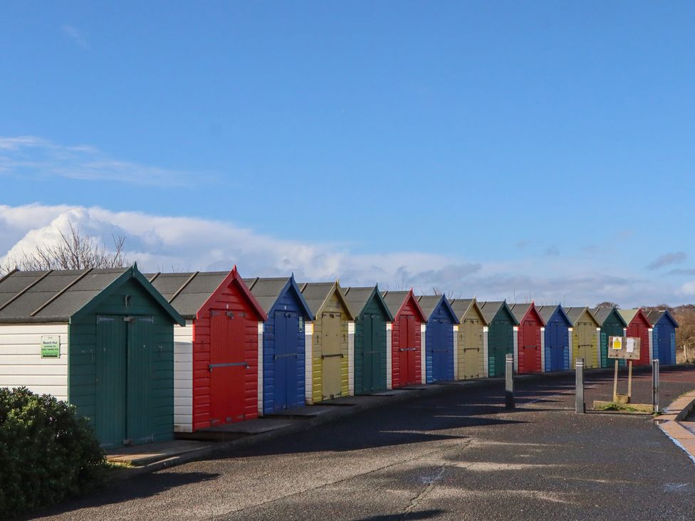 A row of colorful beach huts along a pathway at Flat 1 Lee Cliff Park in Dawlish Warren