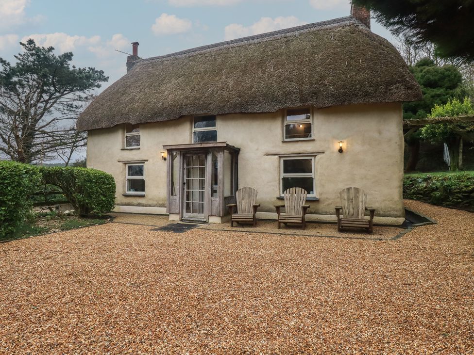 A house with a thatched roof and wooden chairs at Plenteth in Truro