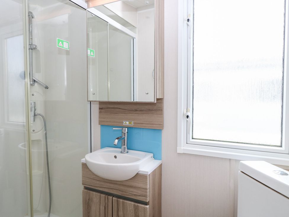 A bathroom with a shower, sink, and mirror at Caravan in Great Yarmouth