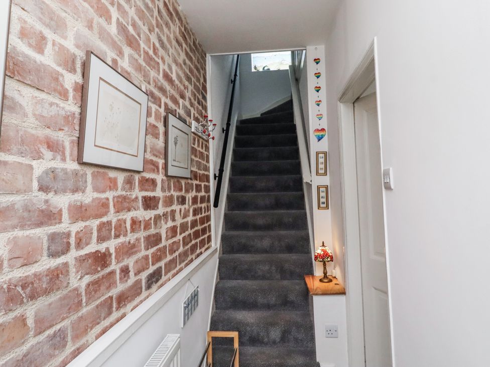 A hallway with a staircase and pictures on the wall at 55 Meldon terrace in Newbiggin-by-the-Sea