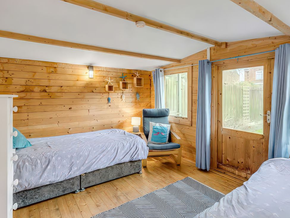 A bedroom with two beds, a chair, and a door at Bay Tree Cottage in Heacham