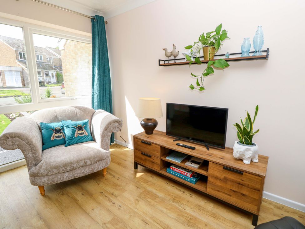 A living room with a chair, television, and decorative items at Camellia Cottage in Wimborne Minster