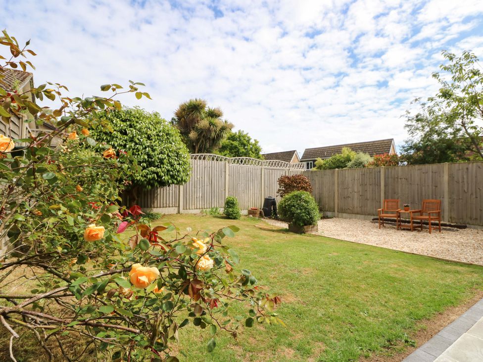 A garden with grass, flowers, a fence, chairs, and a table at Camellia Cottage in Wimborne Minster
