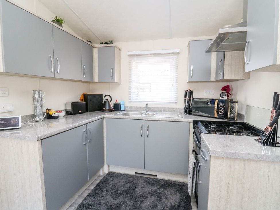 A kitchen with cabinets, sink, stove, and small appliances at 33 Woodpecker Lodge in Llanarth