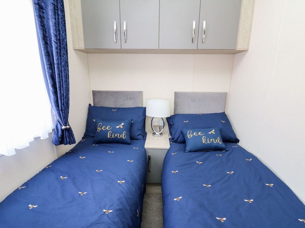 A bedroom with two beds and a bedside table at 33 Woodpecker Lodge Llanarth