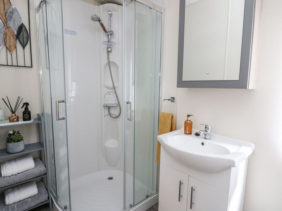A bathroom with a shower, sink, and mirror at 33 Woodpecker Lodge in Llanarth