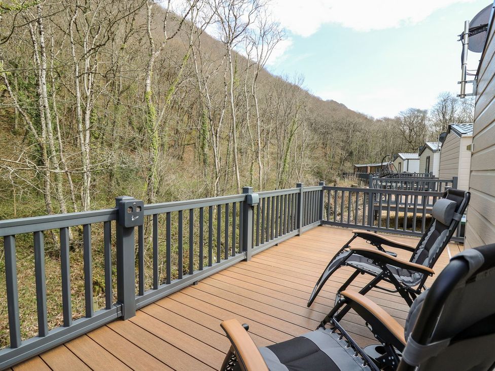 A deck with chairs overlooking a forested area at 33 Woodpecker Lodge Llanarth