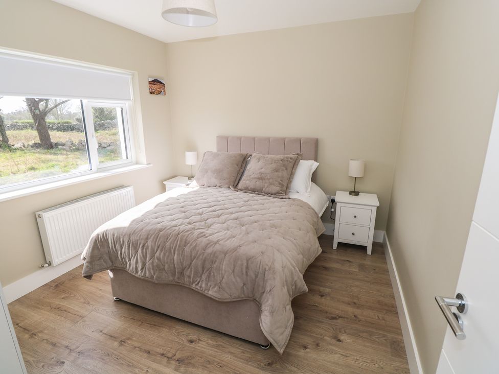A bedroom with a bed, bedside table, and window at Doire Fhatharta Beag in Carraroe, County Galway