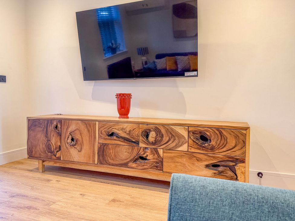 A living room featuring a television mounted on the wall and a wooden sideboard with a vase on it at 4 Bryn Heulog in Wrexham