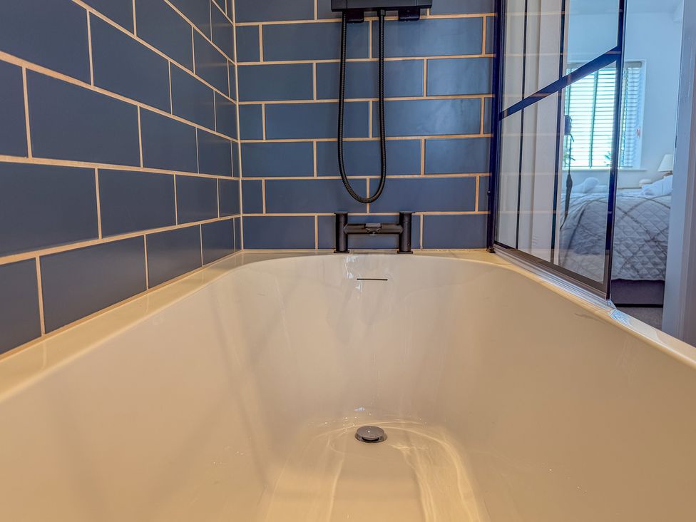 A bathtub with a showerhead and tiled wall at 4 Bryn Heulog in Wrexham