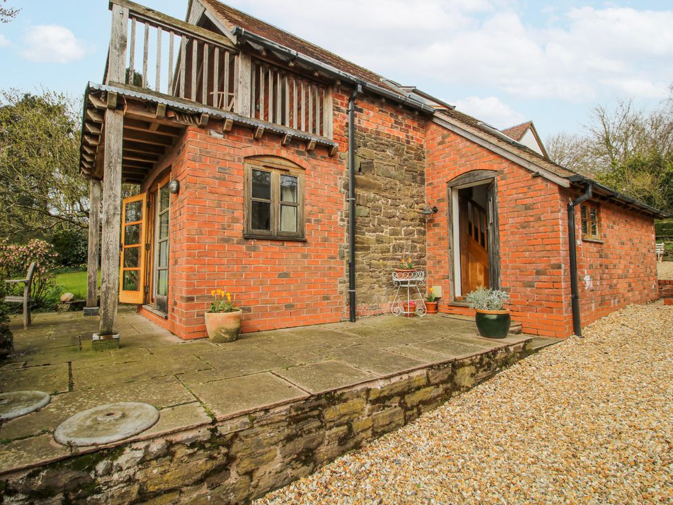 An exterior view of a brick cottage with a patio and flower pots at Bell House Cottage in Wistanstow near Craven Arms