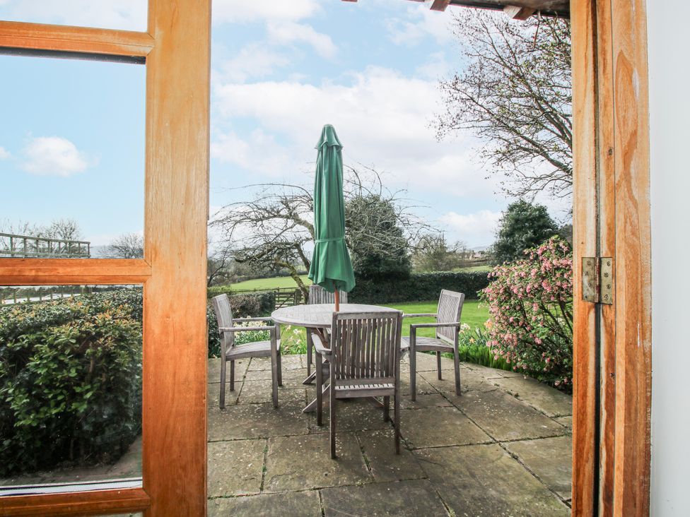 A patio area with a table and chairs under an umbrella at Bell House Cottage in Wistanstow near Craven Arms