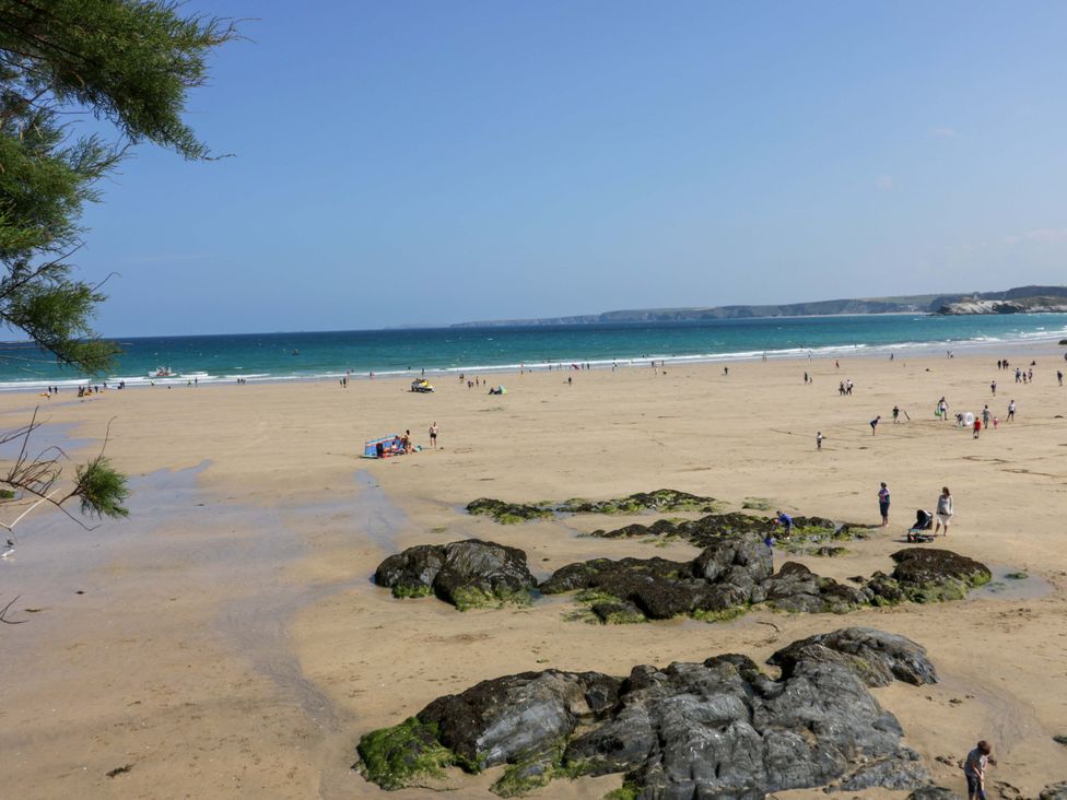 A beach with people walking and boats in the water at Tolcarne Reach in Newquay
