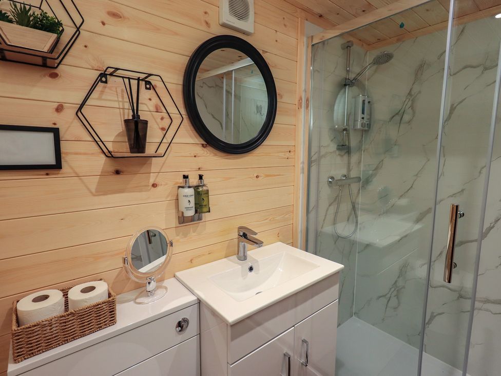 A bathroom with a sink, shower, and wall shelves at Bluebelle - Crossgate Luxury Glamping, Hartsop